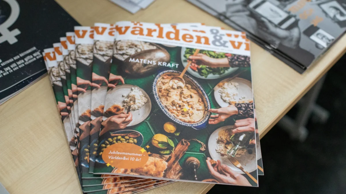 En bunt nummer av tidningen Världen & vi ligger på ett bord. Omslaget visar personer som äter tillsammans runt ett bord. Text på framsidan lyder Matens kraft och Jubiläumsnummer Världen&vi 10 år.