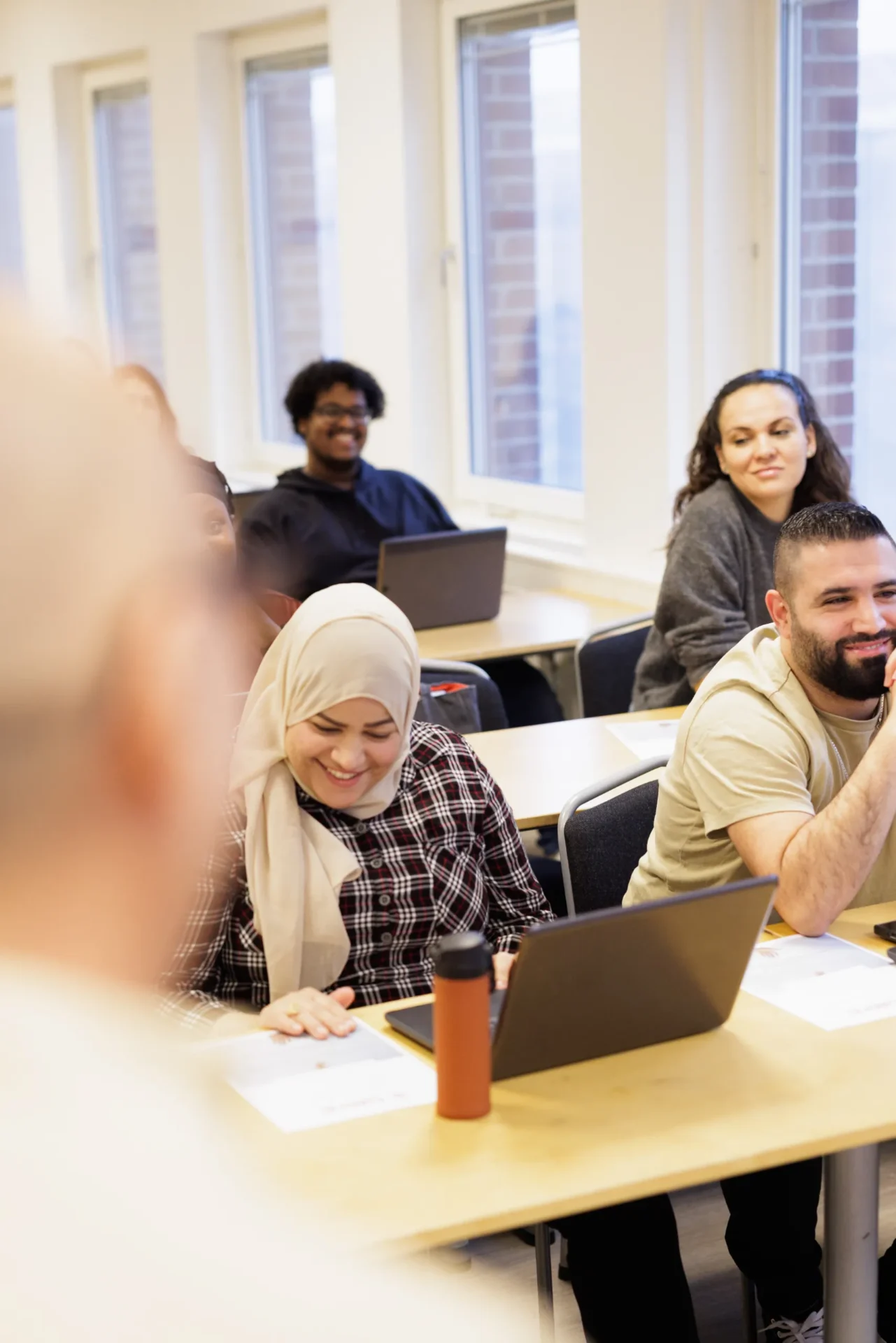 En grupp kursdeltagare sitter i ett klassrum vid sina datorer och skrattar medan läraren står framför dem utanför bild.